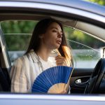 Exhausted,Young,Woman,Driver,With,Hand,Fan,Suffering,From,Heat