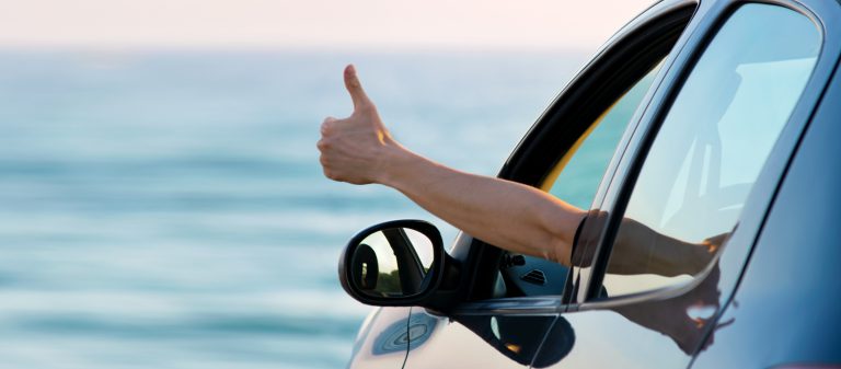 Man,Showing,Thumbs,Up,From,Car,Window,With,Sea,And