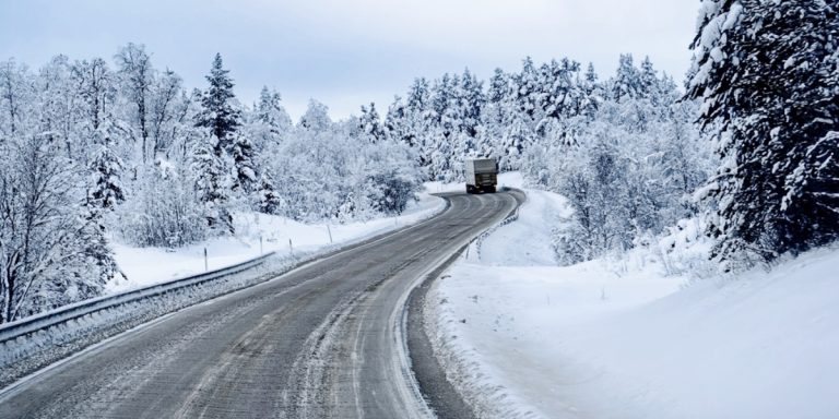 Lone,Truck,Driving,Along,Snowy,Forest,Road,Surrounded,By,Snow-laden